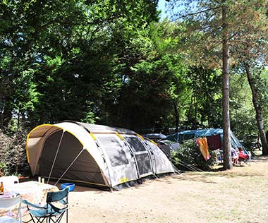 Zelte und Campingmöbel unter den Bäumen des Campingplatzes Le Fief in der Südbretagne